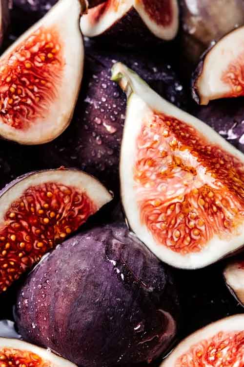 Close-up of fresh figs, including halved figs showing pinkish-red interiors and one whole dark purple fig with water droplets.