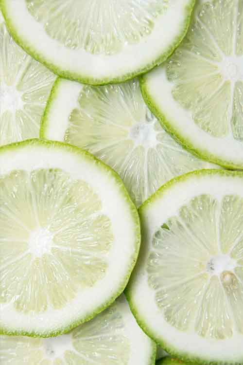 Close-up of overlapping lime slices showing pale green rinds, white pith, and translucent green pulp.