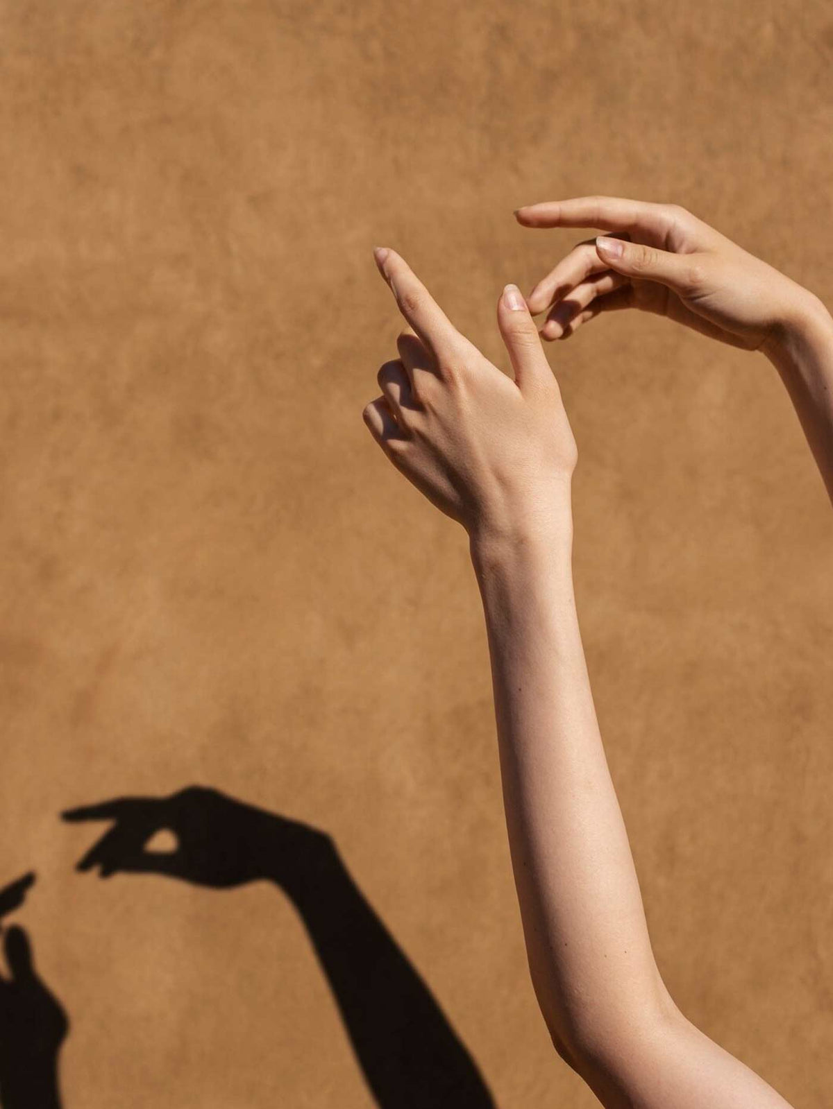 Two hands and forearms posed against a warm tan textured wall, casting a dark shadow.