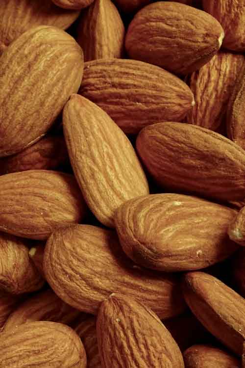 A close-up pile of whole almonds filling the frame, showing their natural brown skin and elongated oval shape.