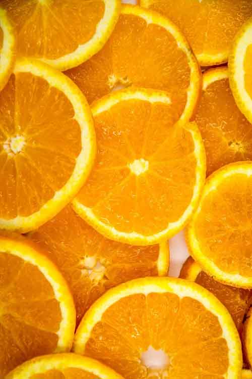 A close-up, top-down view of overlapping orange slices filling the frame, with bright yellow rinds and juicy orange pulp visible.